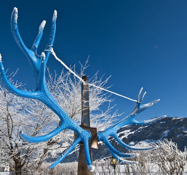 A blue set of antlers stands in the snow in front of Hotel Theresa Zillertal