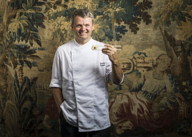 Koch Stefan vom Hotel Theresa im Zillertal präsentiert eine Maki-Rolle vor einem Wandteppich