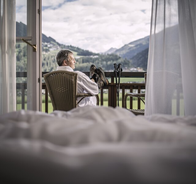 Ein Mann mit Bergschuhen sitzt auf dem Balkon im Zillertaler Hotel Theresa und blickt auf die Berge