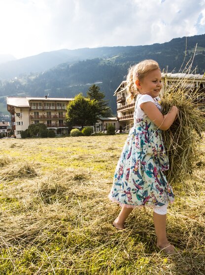 A little girl carries hay in a field in front of the Hotel Theresa in Zillertal