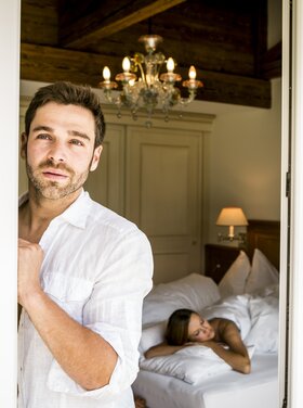 A man stands on the balcony of a room in the Hotel Theresa in Zillertal while a woman lies in bed