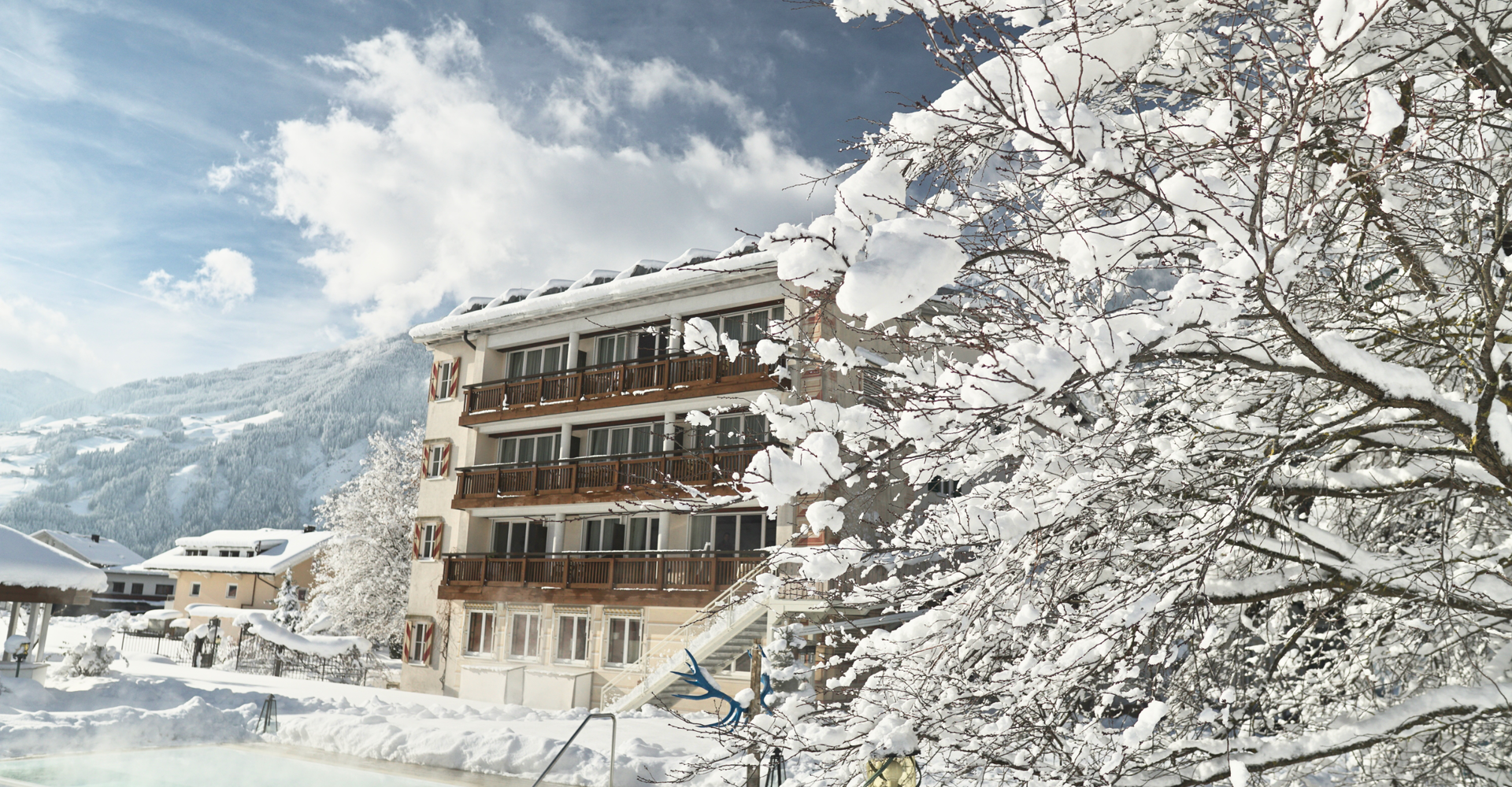 Der verschneite Baumgarten mit Pool des Hotel Theresa im Zillertal zeigt das Hotelgebäude im Hintergrund