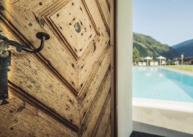 Ein hölzernes Tor mit einem alten Griff führt zum Sauna- und Poolbereich des Hotel Theresa im Zillertal