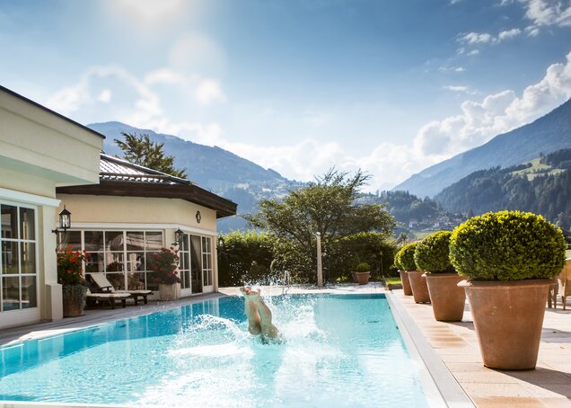 Someone jumps into the water in front of a mountain backdrop at the Zillertal Hotel Theresa