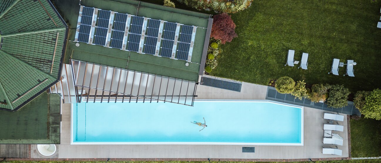 Drone shot shows a person swimming in the outdoor pool of the Wellnesshotel Theresa in Zillertal