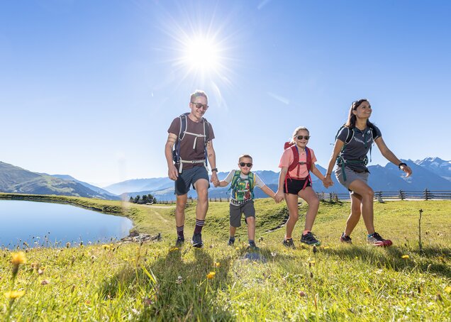 A family hikes past a small lake on the Isskogel in the Zillertal Arena
