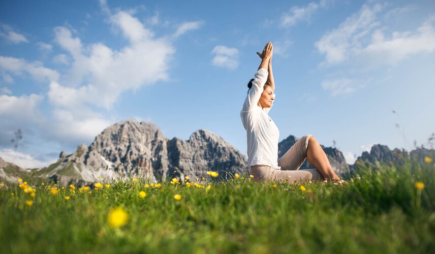 Eine Frau macht Yoga auf einer Wiese vor einer Bergkulisse im Hotel Theresa im Zillertal