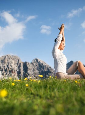 A woman does yoga on a meadow in front of a mountain backdrop at the Hotel Theresa in Zillertal