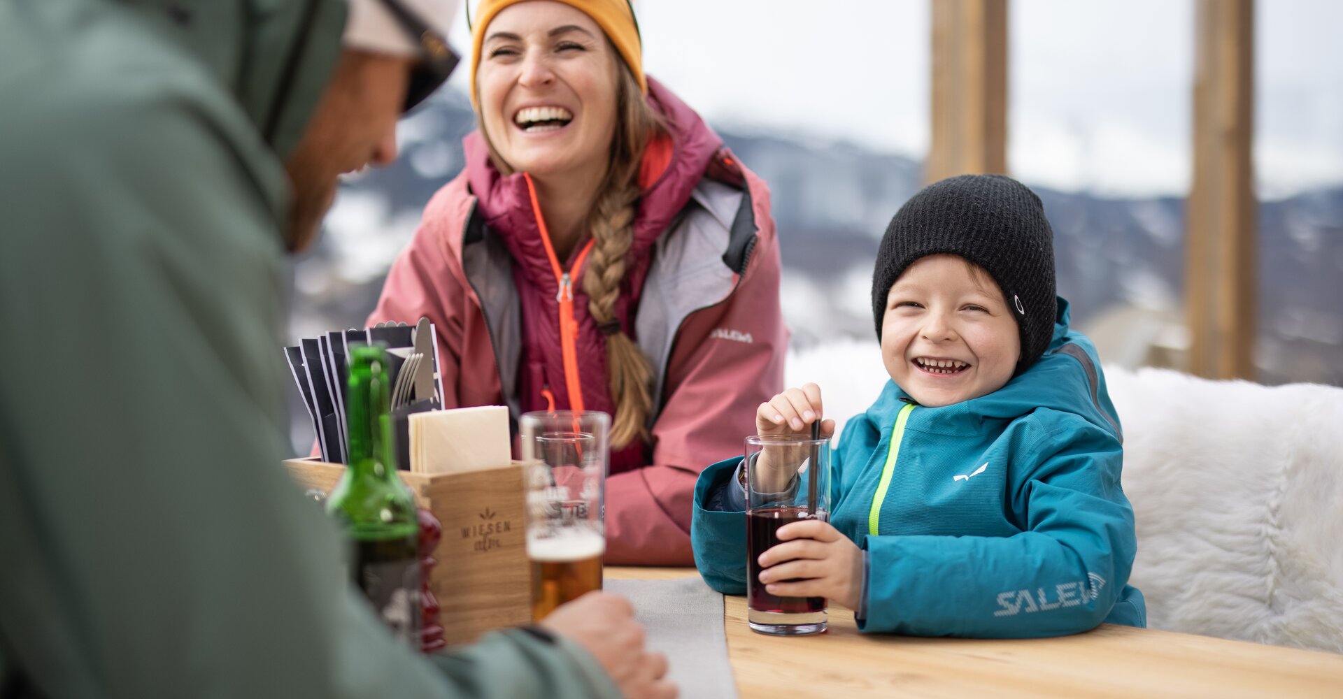 A family sits laughing at a table on a mountain hut terrace