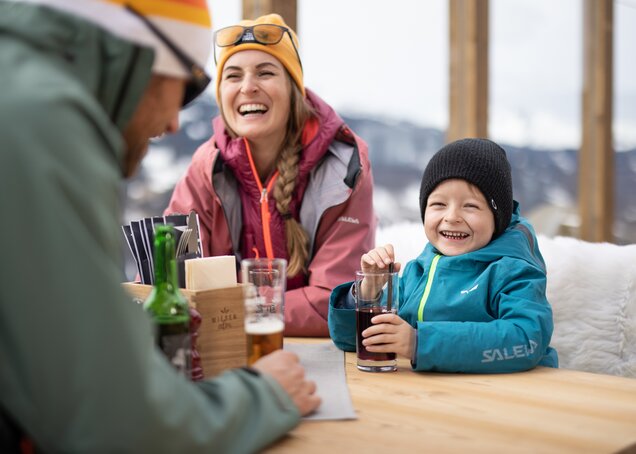 A family sits laughing at a table on a mountain hut terrace