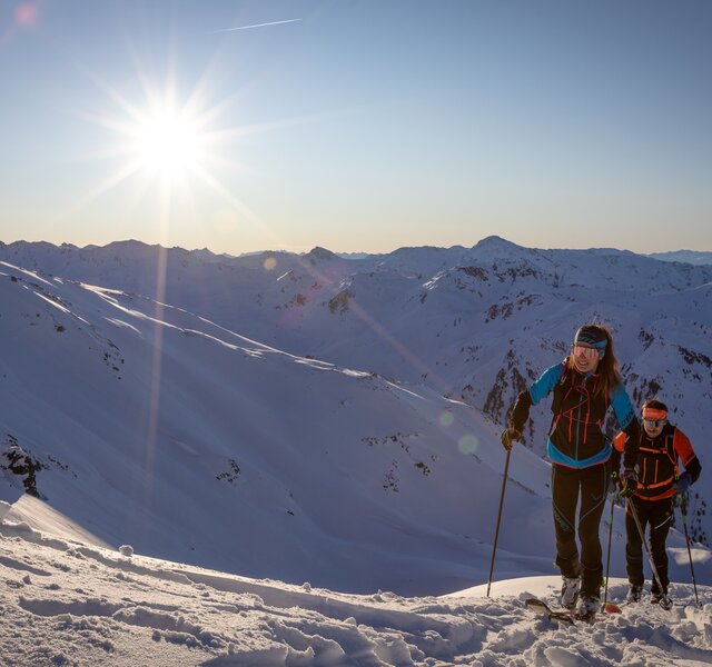 Zwei Skitourengeher steigen in strahlendem Sonnenschein einen schneebedeckten Hang hinauf