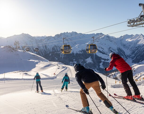 Skifahrer fahren eine verschneite Piste unter einer Seilbahn hindurch hinunter